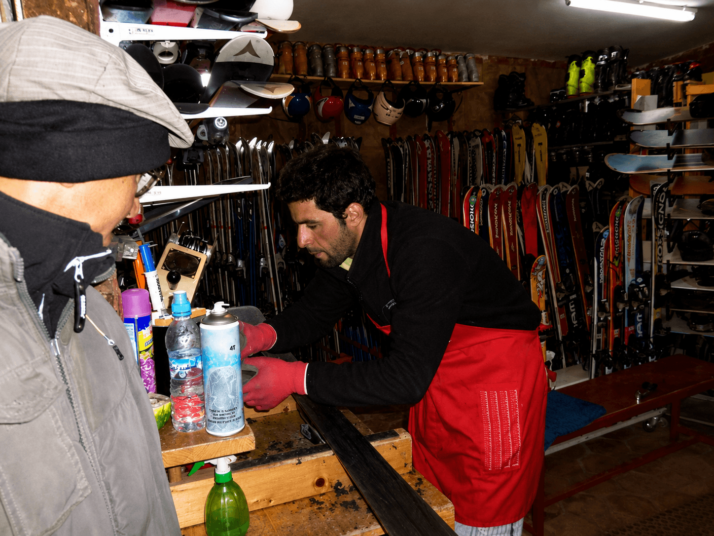 Un technicien d’Univers Glisse farte un ski sur l’établi de l’atelier, devant les racks de skis et de chaussures du magasin