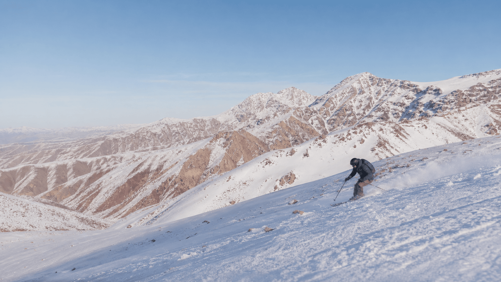 Skieur descendant une pente enneigée dans un paysage inspiré du Haut Atlas