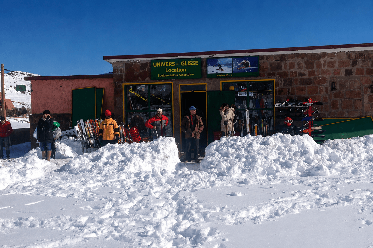 Façade du magasin de location de ski Univers Glisse à l’Oukaïmeden, skis et snowboards alignés devant l’entrée sous la neige