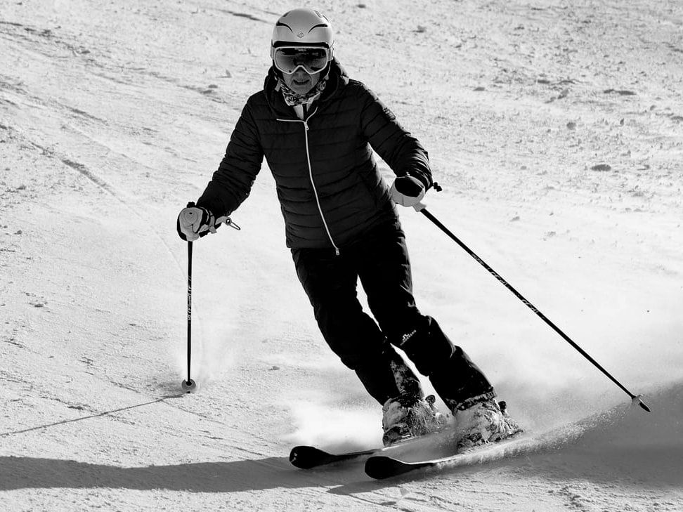 Skieuse en virage sur une piste damée, gerbe de neige derrière ses skis