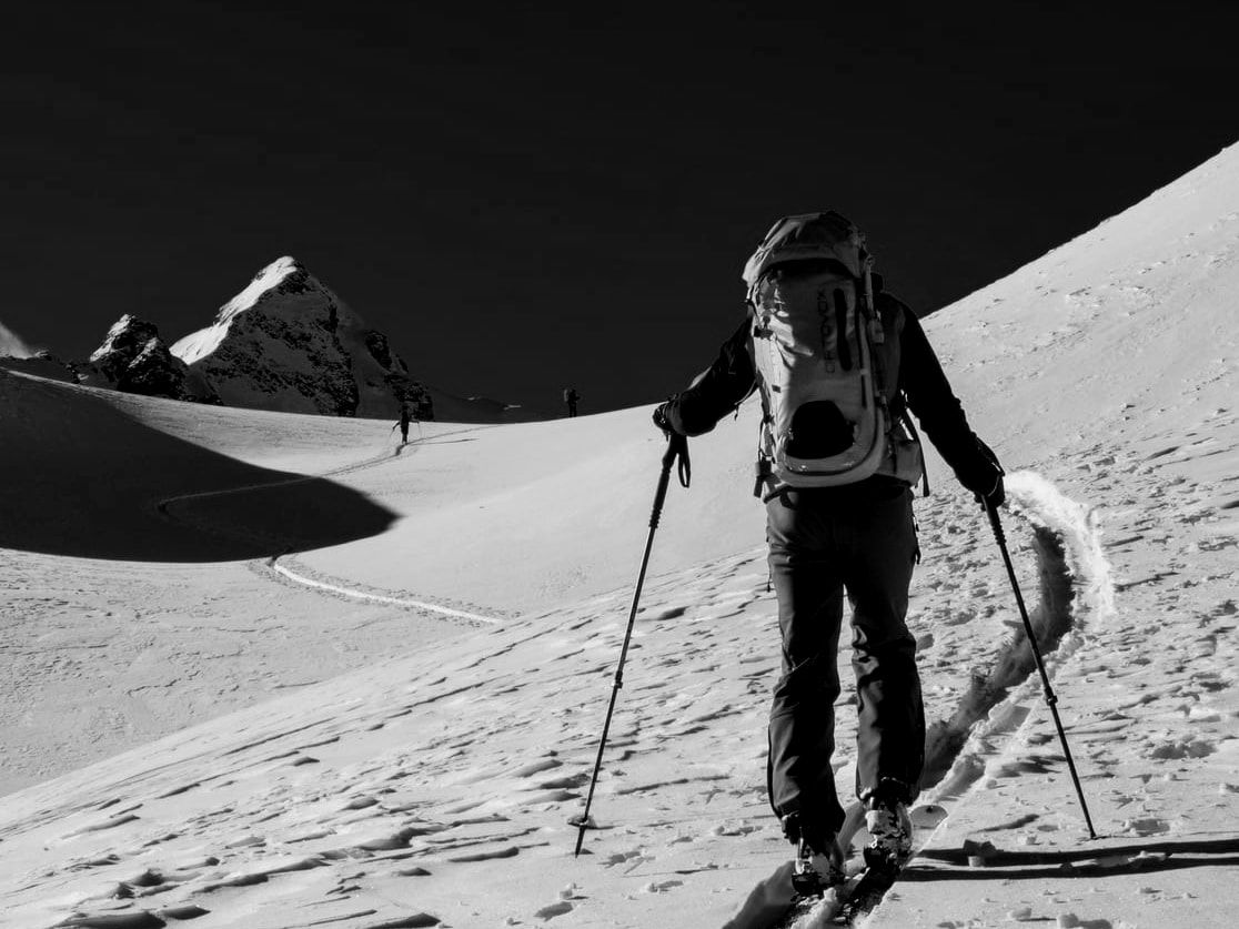 Skieur de randonnée montant une pente vierge vers un sommet enneigé