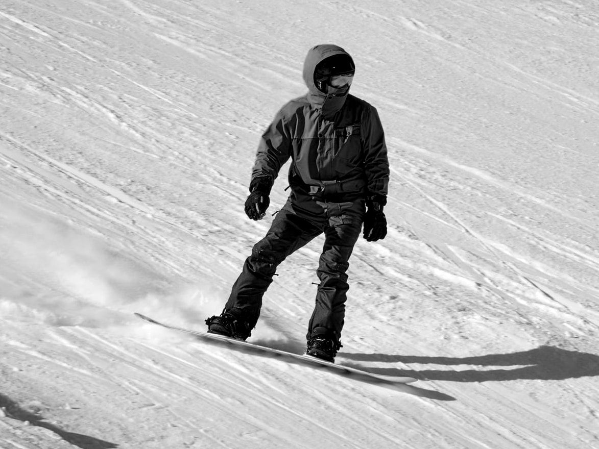 Snowboardeur en descente sur une large piste enneigée